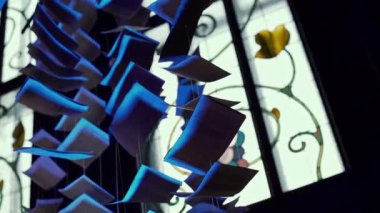 Tavandan sarkan sayfalar dolusu kitaplardan yapılmış mavi renkli çelenkler. Performans