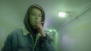 Kısa saçlı bir kadın alt geçitte sigara içiyor..