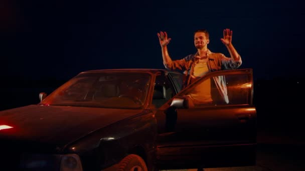 Az ember éjjelente táncol, ugrál és integet a kocsihoz nyitott ajtóval.. — Stock videók