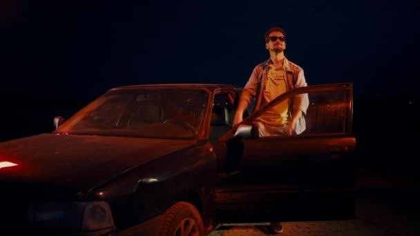 Man at night dances, jumps and waves his hands near the car with the door open. — Stock Video