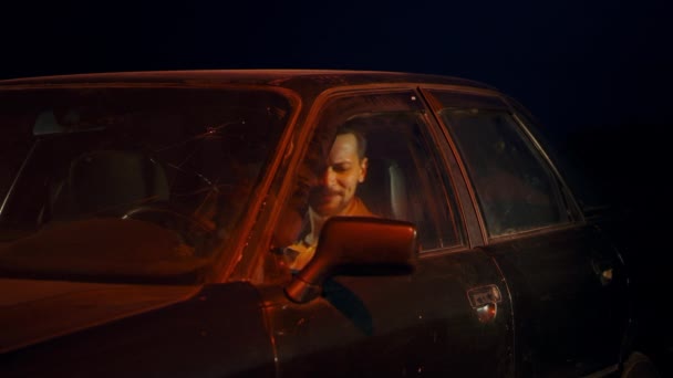 Кавказский мужчина сидит ночью в машине с открытой дверью и танцует под музыку — стоковое видео