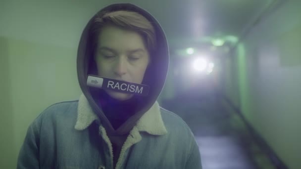 Frau in Kapuze und Jeansjacke hält ein Schild mit der Aufschrift - RACISM — Stockvideo