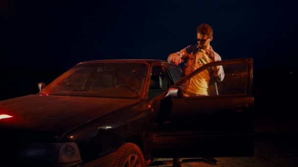 Az ember éjjelente táncol, ugrál és integet a kocsihoz nyitott ajtóval.. — Stock videók