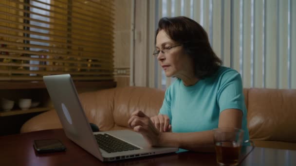Ältere Frau arbeitet am Laptop und tippt abends etwas auf die Tastatur — Stockvideo