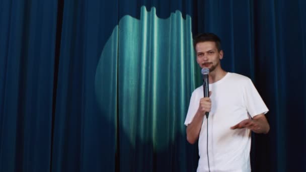 Kerl in weißem T-Shirt auf der Bühne vor blauem Stoffhintergrund — Stockvideo
