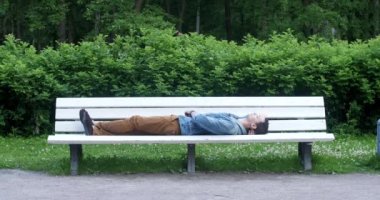Adam parkta yorgun ve uyumak için bir bankta uzan.