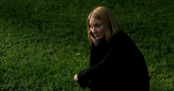 Dívka dřepy a mluví po telefonu v parku. — Stock video