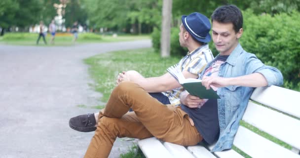 Twee jongens zijn zittend op een bankje en praten. Guy gevraagd hoe laat is het nu. — Stockvideo