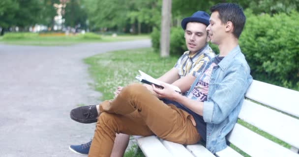 Dva chlapi sedí na lavičce a mluví. Mluví o knize. — Stock video