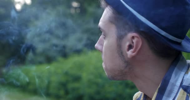 Парень-хипстер курит в парке — стоковое видео