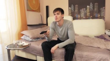 Yatağın üzerine oturan, Tv izlerken ve uzak tutan adam