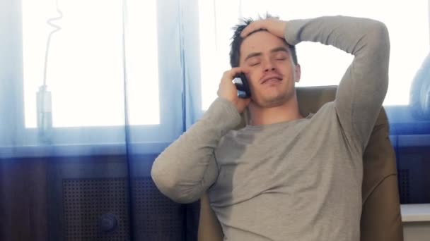 Взрослый мужчина сидит в кресле и разговаривает по телефону — стоковое видео