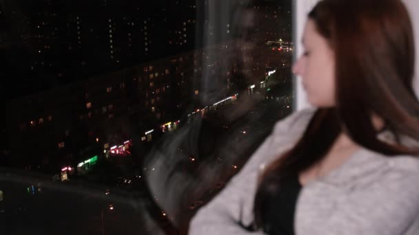 悲しい女性は座っている窓の下枠上見て夜の街で — ストック動画