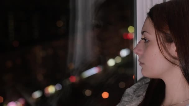 悲しい女性は座っている窓の下枠上見て夜の街で — ストック動画