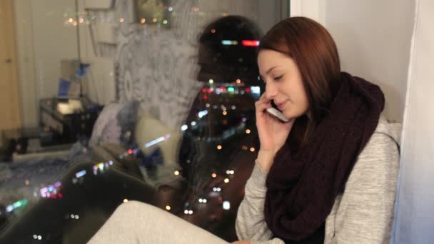 Chica se sienta en el alféizar de la ventana y hablando por teléfono — Vídeos de Stock