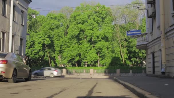 Vista de la calle con parque verde y coches en el día de verano. Pareja de ciclismo en una carretera — Vídeos de Stock