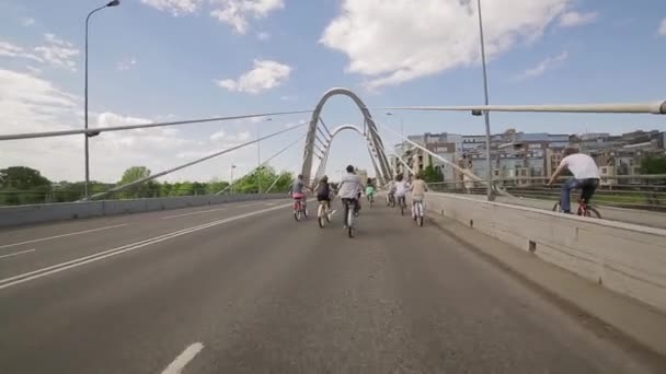 Задняя сторона велосипедной группы людей, пересекающих мост в летний день облачности . — стоковое видео