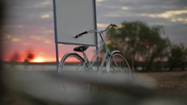 Blauwe fiets blijft op het uithangbord op een strand in de zomer zonsondergang. Horizontale pan. — Stockvideo