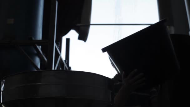 Ouvrier ajouter des grains de café non frits dans un grand fût rond en aluminium dans une usine de café 