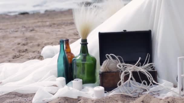 Decorative bottles stand on white tissue with candles, box of threads. Beach. — Stock Video