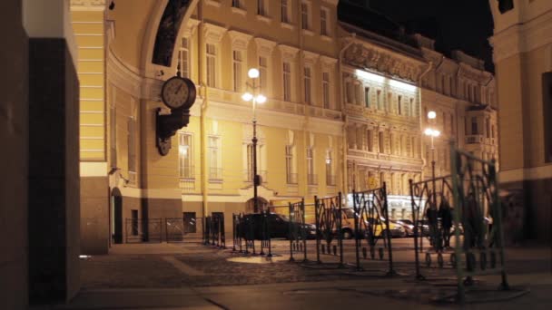 Weergave street met verlichte gebouwen, horloge, hek en mensen in de nacht. — Stockvideo