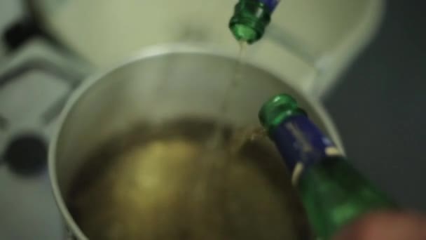 Handen giet water uit twee flessen in grote aluminium pan op gas-kookplaat. — Stockvideo