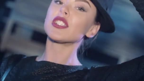 Привлекательная девушка в черном топ-танце, играет со шляпой в ночном клубе. Улыбнись на камеру — стоковое видео