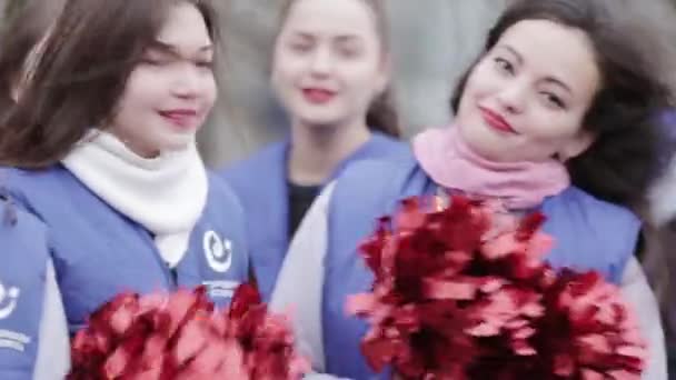 SAINT PETERSBURG, RUSSIA - NOVEMBER 28, 2015: Attractive cheerleaders in blue jackets smile in camera. Red shakers. Outdoor — ストック動画