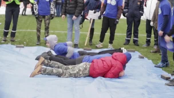 SAINT PETERSBURG, RUSSIA - NOVEMBER 28, 2015: Young boys lie on blue tarpaulin, stand on command. Emercom training. Audience — Stock Video