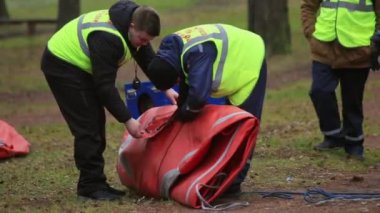 SAINT PETERSBURG, RUSSIA - NOVEMBER 28, 2015: Two men in rescue uniform unfolded orange tent in forest. Emercom camping