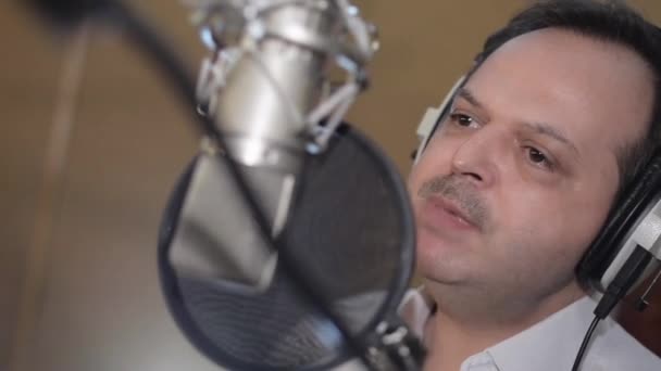 Porträt eines Mannes, der ruhig mit Kopfhörern vor dem Mikrofon singt. Studio. — Stockvideo