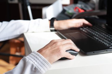 Close-up of a man's hands working with a laptop and a mouse