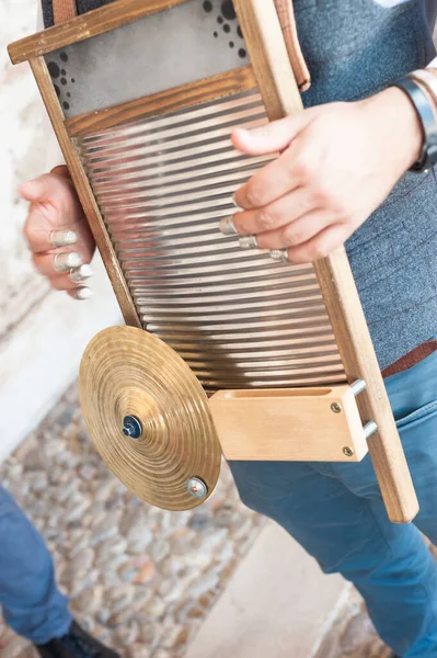 Close-up of a man playing a jazz instrument on a washboard in the street. The instrument is seen, along with the cymbal, the wood and the thimbles with which it is played.