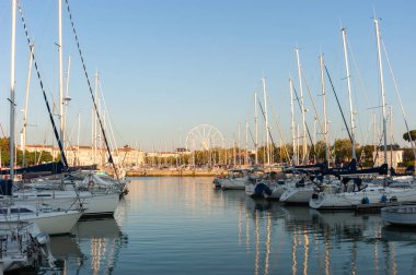 La Rochelle, Fransa; 10 Ağustos 2021: Gemiler Fransa 'nın eski ortaçağ limanı La Rochelle' e yanaştı ve suya yansıdı. Arka planda akşam ışığı tarafından aydınlatılmış bir dönme dolap var..