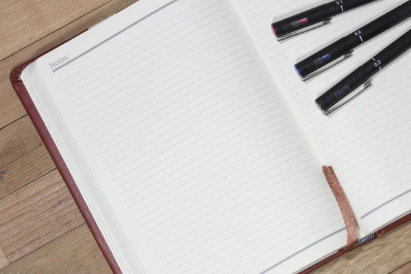 Drei Stifte auf Notizbuch auf Holztisch, Geschäftskonzept — Stockfoto