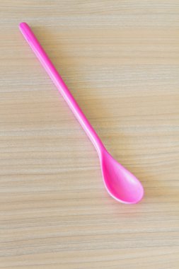 Ahşap arka plan üzerinde uzun pembe plastik kaşık