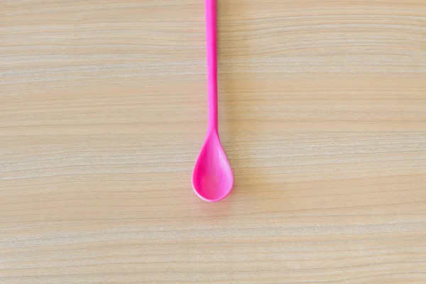 Long pink plastic spoon on wooden background — Stock Photo, Image