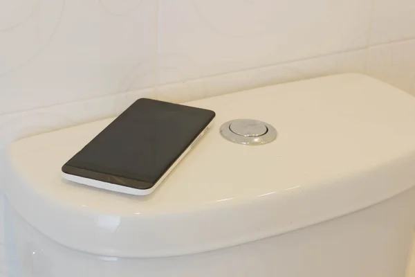 Teléfono inteligente en un inodoro blanco en un baño —  Fotos de Stock