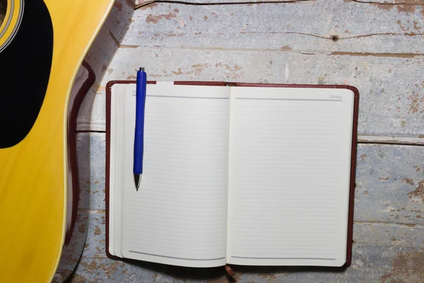 Notatnik i niebieski długopis z gitarą na stare drewniane tła, pisanie muzyki — Zdjęcie stockowe