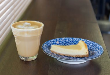 Peynirli kek parçası üzerinde beyaz tablo sütlü kahve fincan.