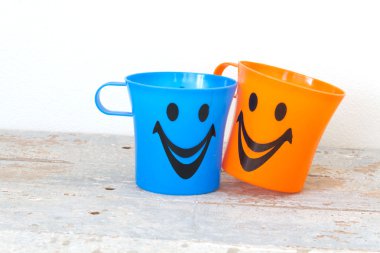 Çeşitli renk ahşap arka plan üzerinde gülümseyen, plastik bardak