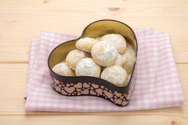 Pamuk damalı peçete üzerinde kalp şeklinde bir teneke içinde küçük kurabiye kutusu