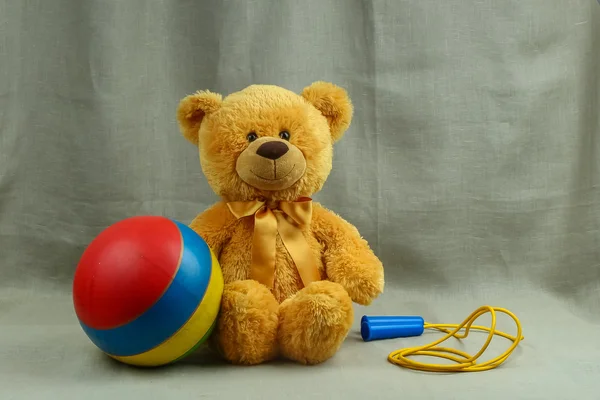 Помаранчевий усміхнений іграшковий ведмідь зі смугастим м'ячем і мотузкою — стокове фото