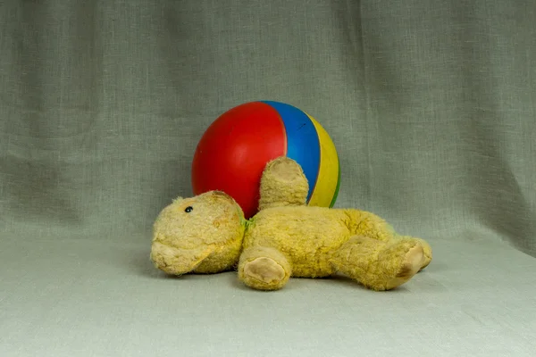 Старий жовтий плюшевий ведмідь зі смугастим м'ячем — стокове фото