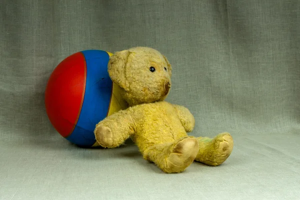 Старий старовинний жовтий плюшевий ведмедик зі смугастим м'ячем — стокове фото