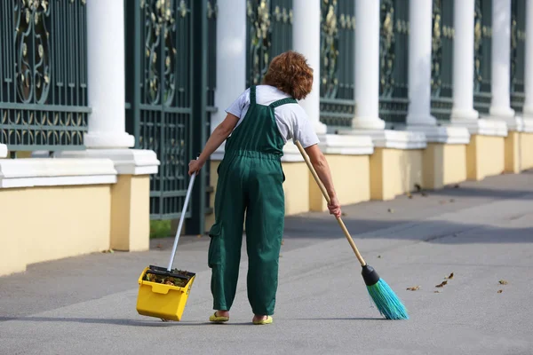 Inserviente pulisce il marciapiede della città dalle foglie cadute — Foto Stock