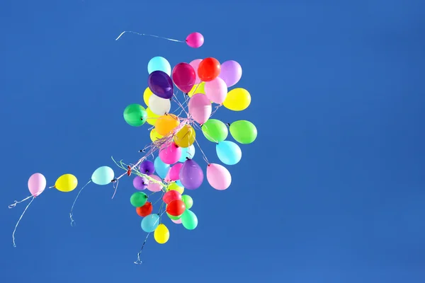 Viele bunte Ballons fliegen in den blauen Himmel — Stockfoto