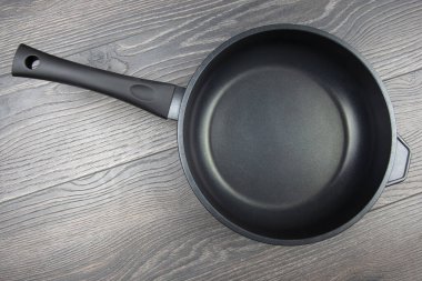 Ahşap arka planda yapışmayan teflon kaplamalı siyah tava.