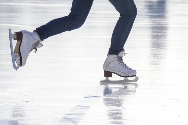 legs of a woman in blue jeans and white skates on an ice rink. hobbies and leisure. winter sport