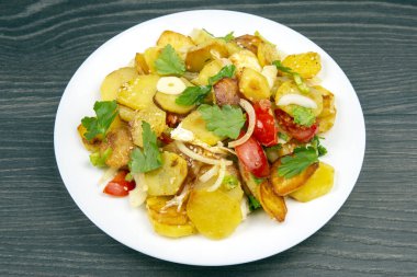 Tahta bir masada, beyaz bir tabakta, sebze ve otlarla pişirilmiş patates kızartması.